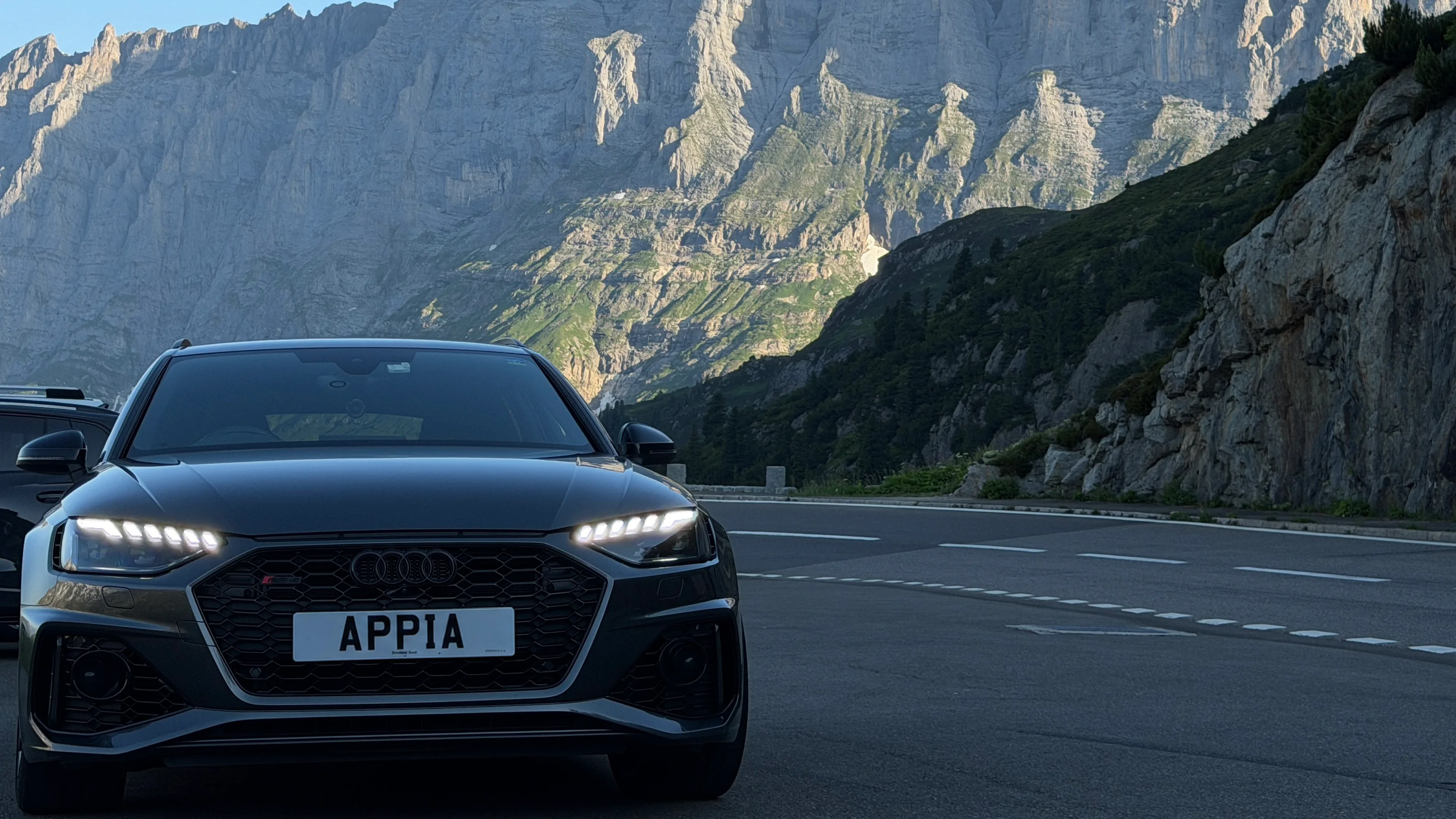An Audi on an Alpine road beneath a dramatic mountain landscape